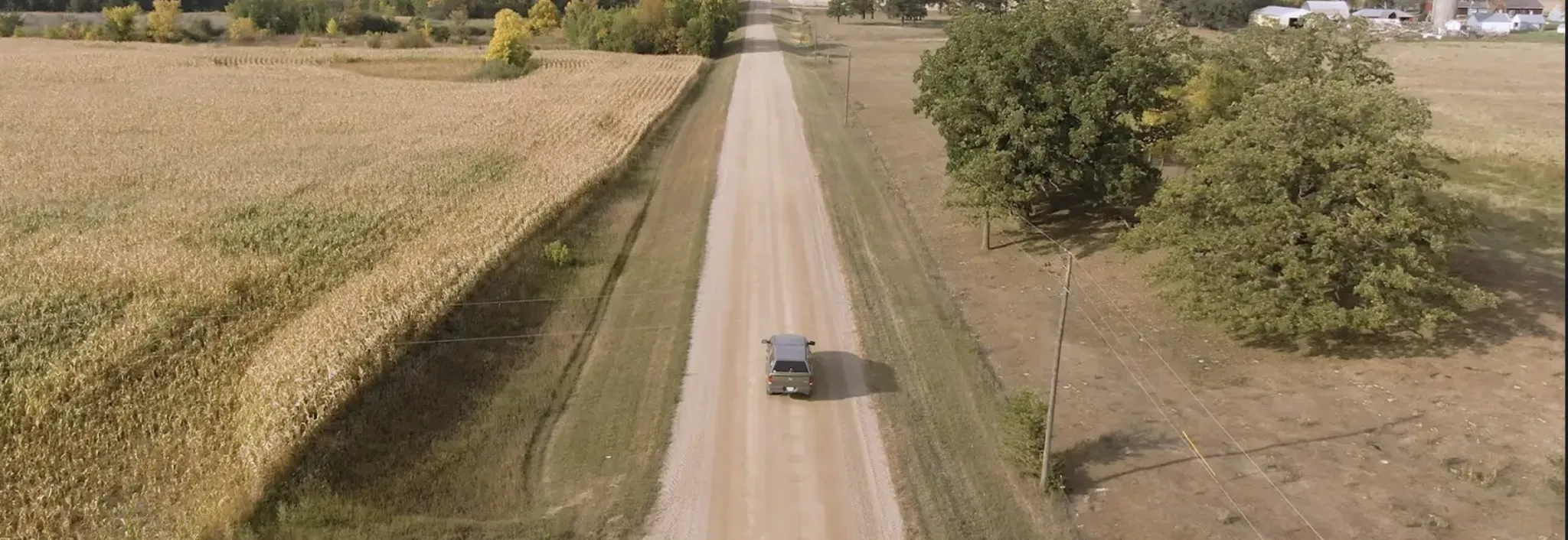 Car driving down a country road past the field of crops. 